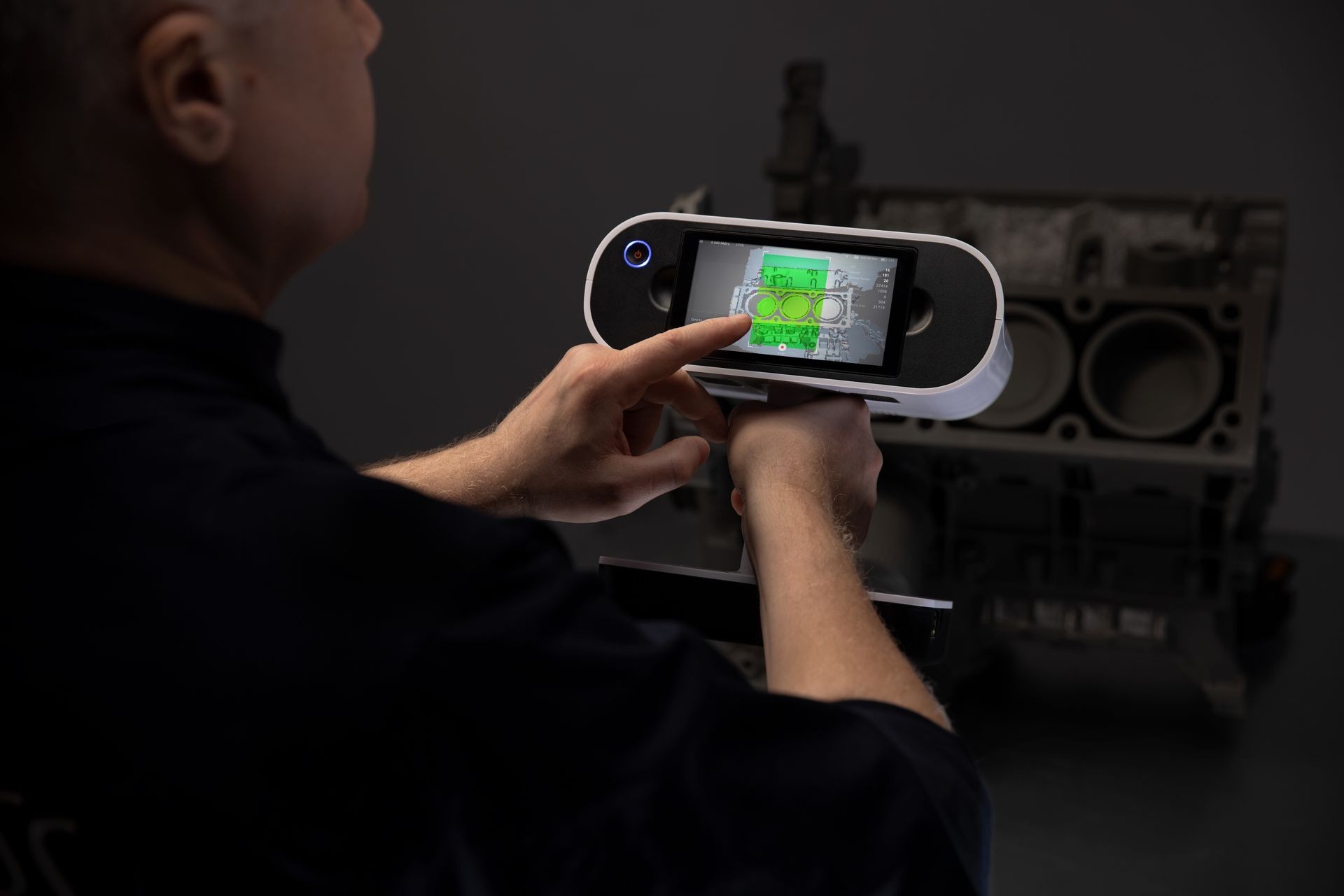 Person using a handheld 3D scanner on a car engine block.